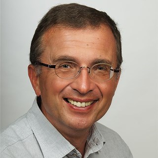 Lächelnder Mann mit braunen Haaren und Brille, der ein graues Hemd trägt