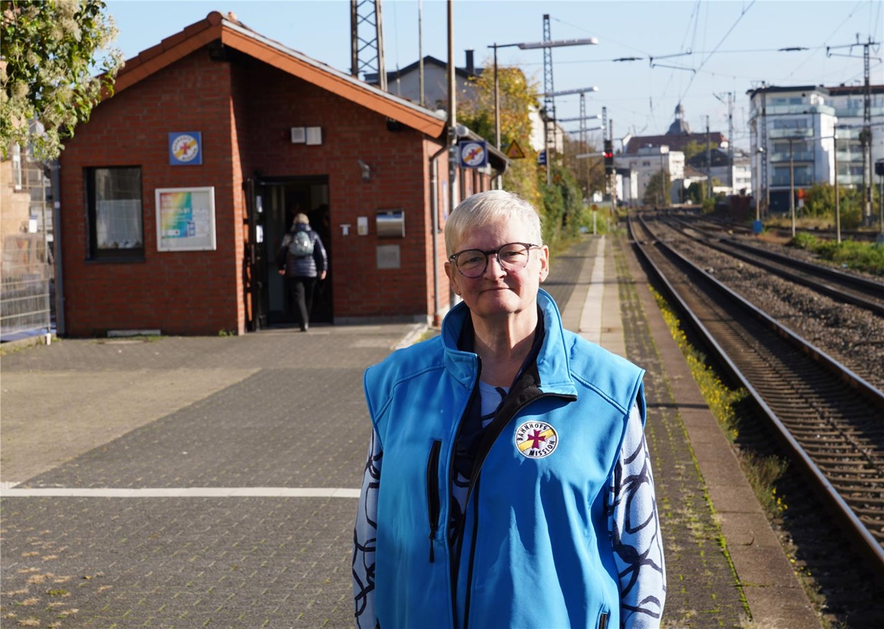 Eine ältere Frau mit blauer Arbeitskleidung auf einem Bahnsteig