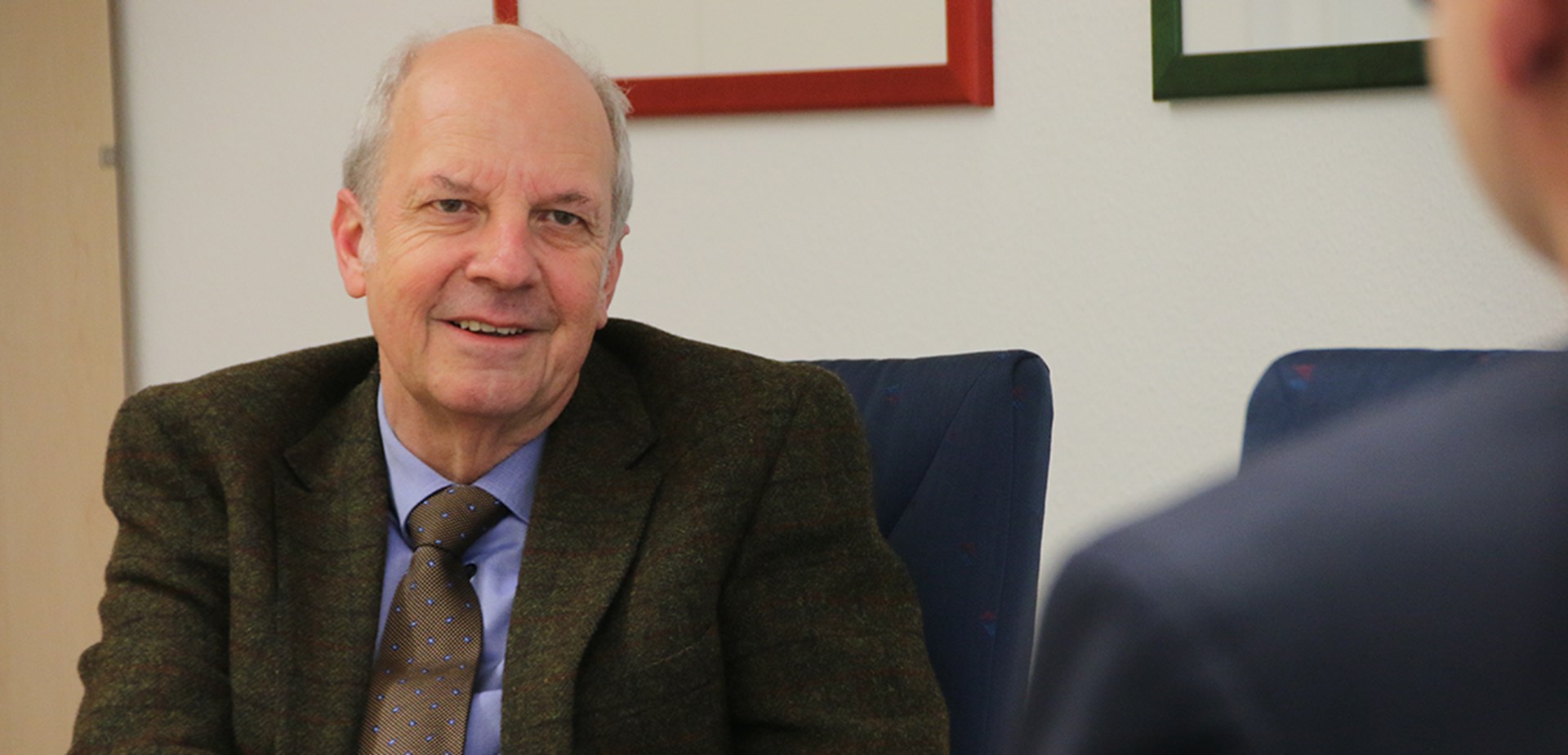 Ein Mann sitzt an einem Besprechungstisch vor einem Tischmikrofon und blickt lächelnd in Richtung des Interviewers