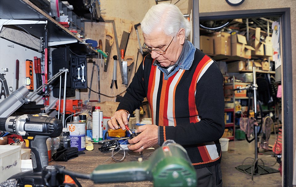 Ein Mann in einem gestreiften Pullover steht in einer Werkstatt an einer Werkbank und arbeitet
