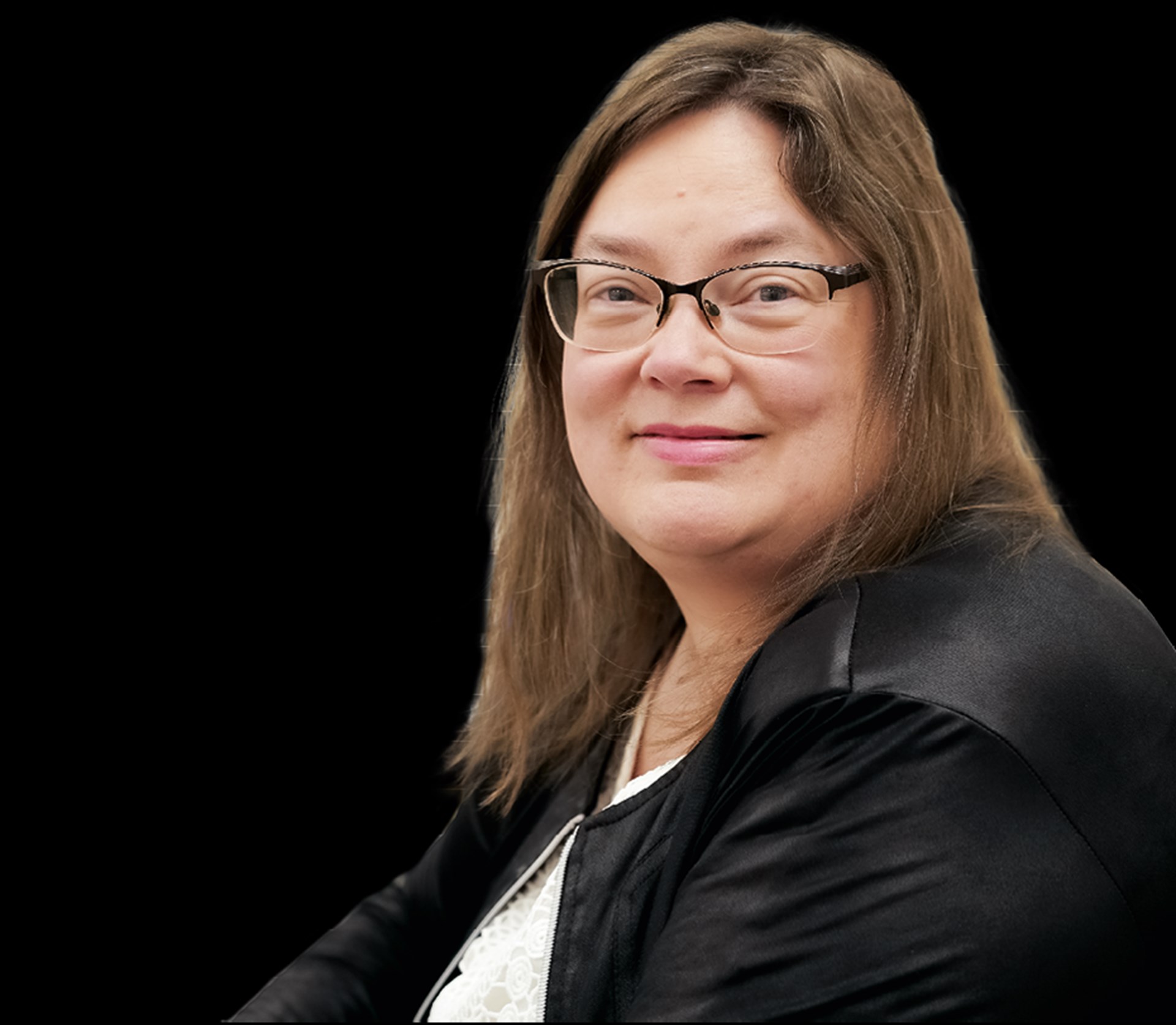 Eine lächelnde Frau mit schulterlangen, blonden Haaren und Brille, die ein weißes Shirt und eine schwarze Jacke trägt