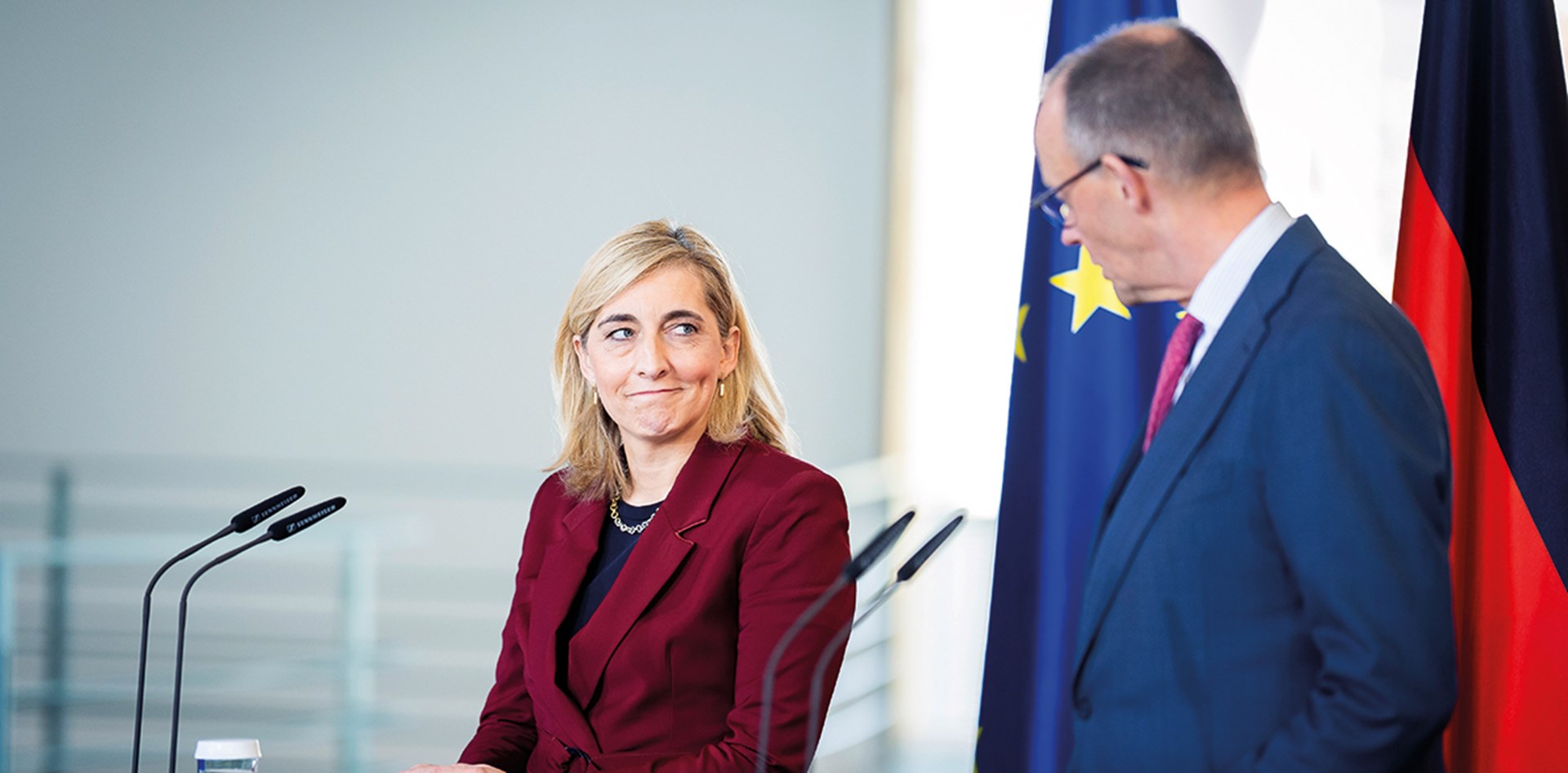 Bundesgesundheitsministerin Nina Warken und Bundeskanzler Friedrich Merz stehen bei einer Pressekonferenz an Rednerpulten und blicken sich dabei in die Augen. Nina Warken lächelt dabei. Hinter ihnen steht eine EU- und eine Deutschland-Flagge.