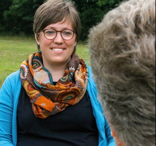 Zwei Frauen die sich auf einem Außengelände in einem Beratungsgespräch befinden. Von der Klientin ist nur der Hinterkopf zu sehen.
