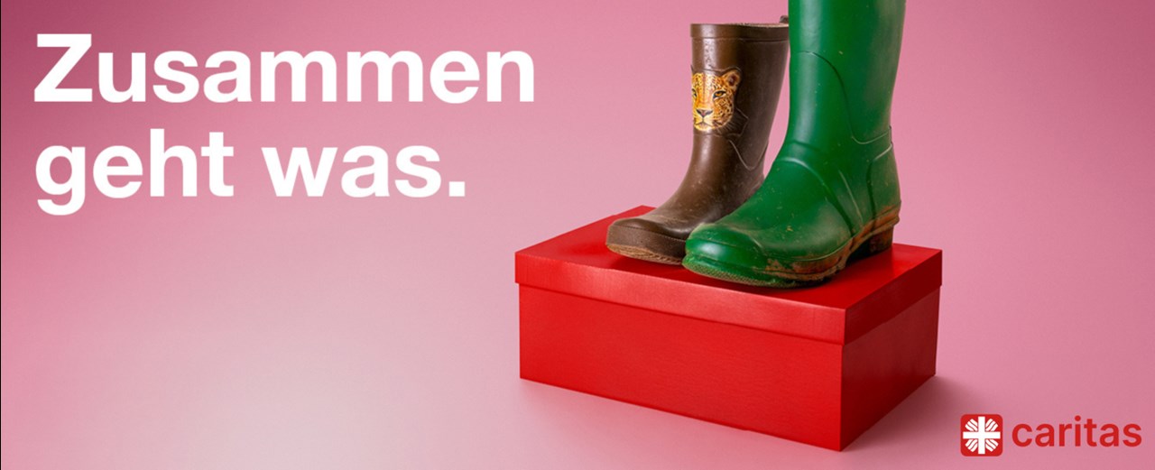 Auf einem roten Schuhkarton sind vor einem rosa Hintergrund ein Paar Gummistiefel zu sehen. Der linke Schuh ist ein brauner Kindergummistiefel mit einem Tigerkopf in kleiner Schuhgröße, der rechte ein hoher grüner Gummistiefel in großer Schuhgröße. Darüber steht das Kampagnenmotto: Zusammen geht was. 
