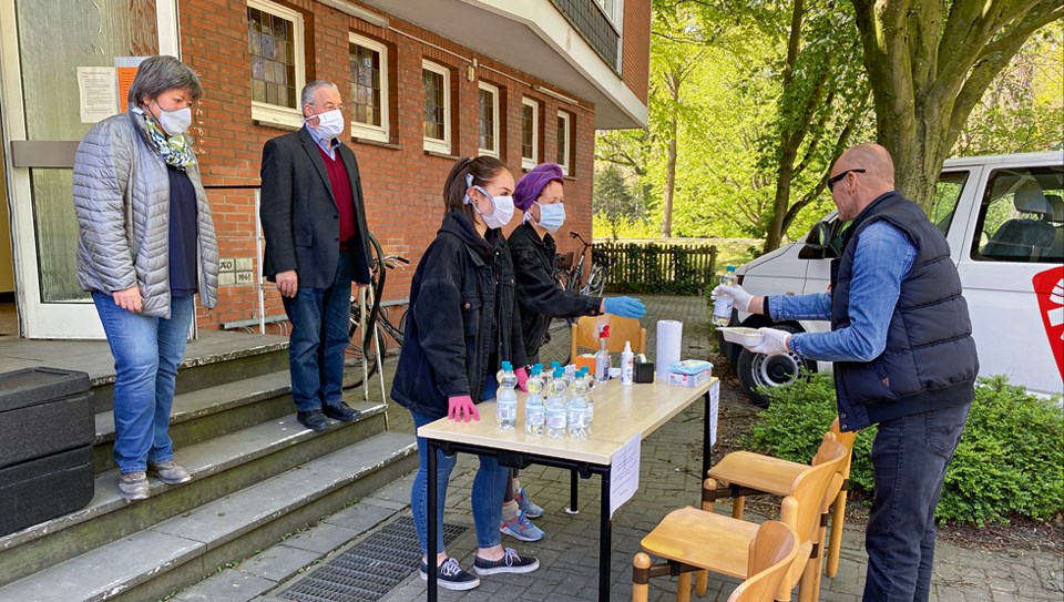 Einige Mitarbeitende von der Caritas und einer Pfarrgemeinde, die vor einem Gebäudeeingang an einer improvisierten Suppenküche mit einem Tisch, einigen Stühlen und Lebensmitteln stehen.