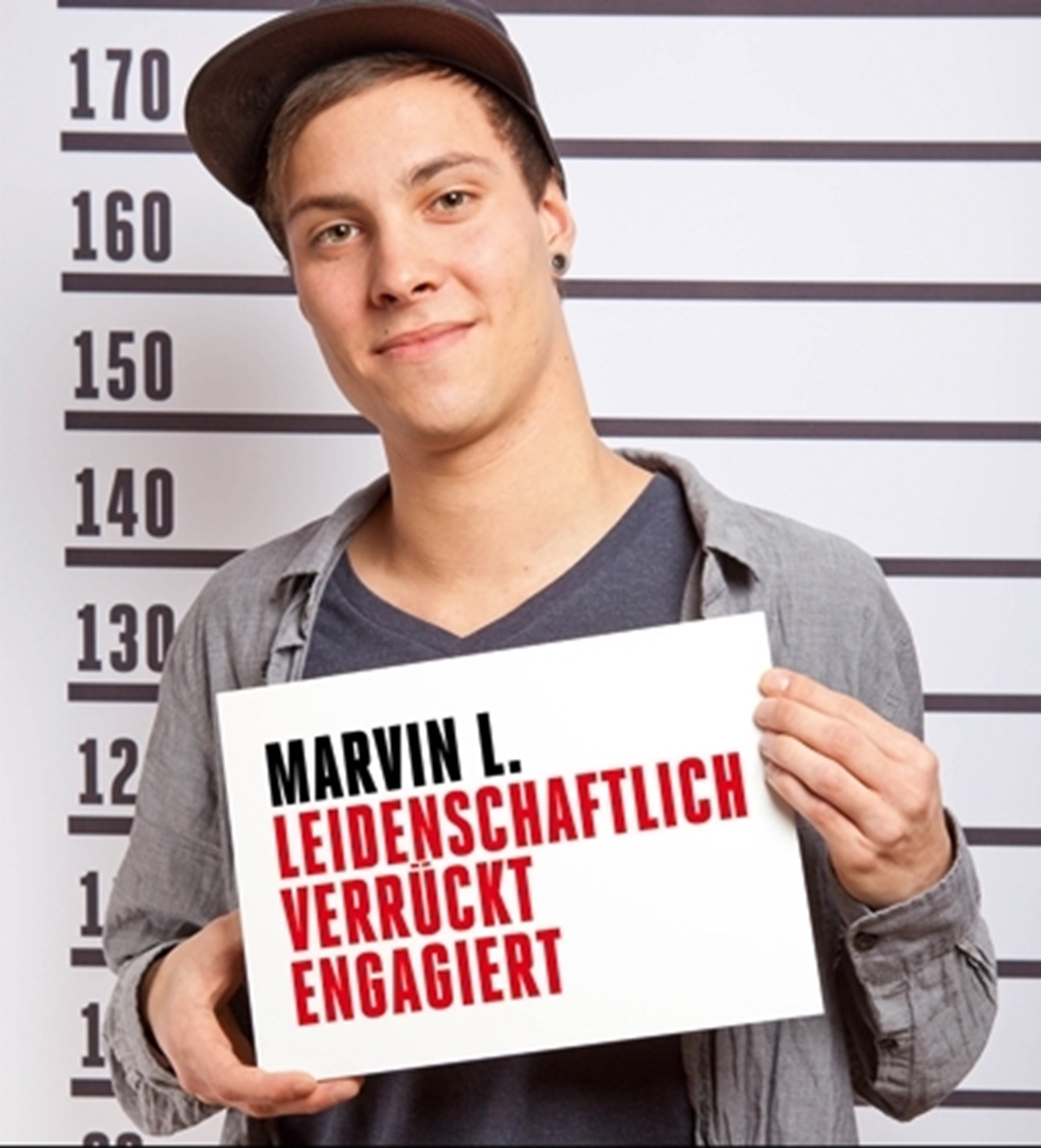 Plakatmotiv zur Kampagne 'CARITÄTER - Täter mit Profil' mit einem lächelnden, jungen Mann vor einer Größen-Skala mit einem Schild. Auf dem Schild steht: Marvin L. - leidenschaftlich - verrückt - engagiert