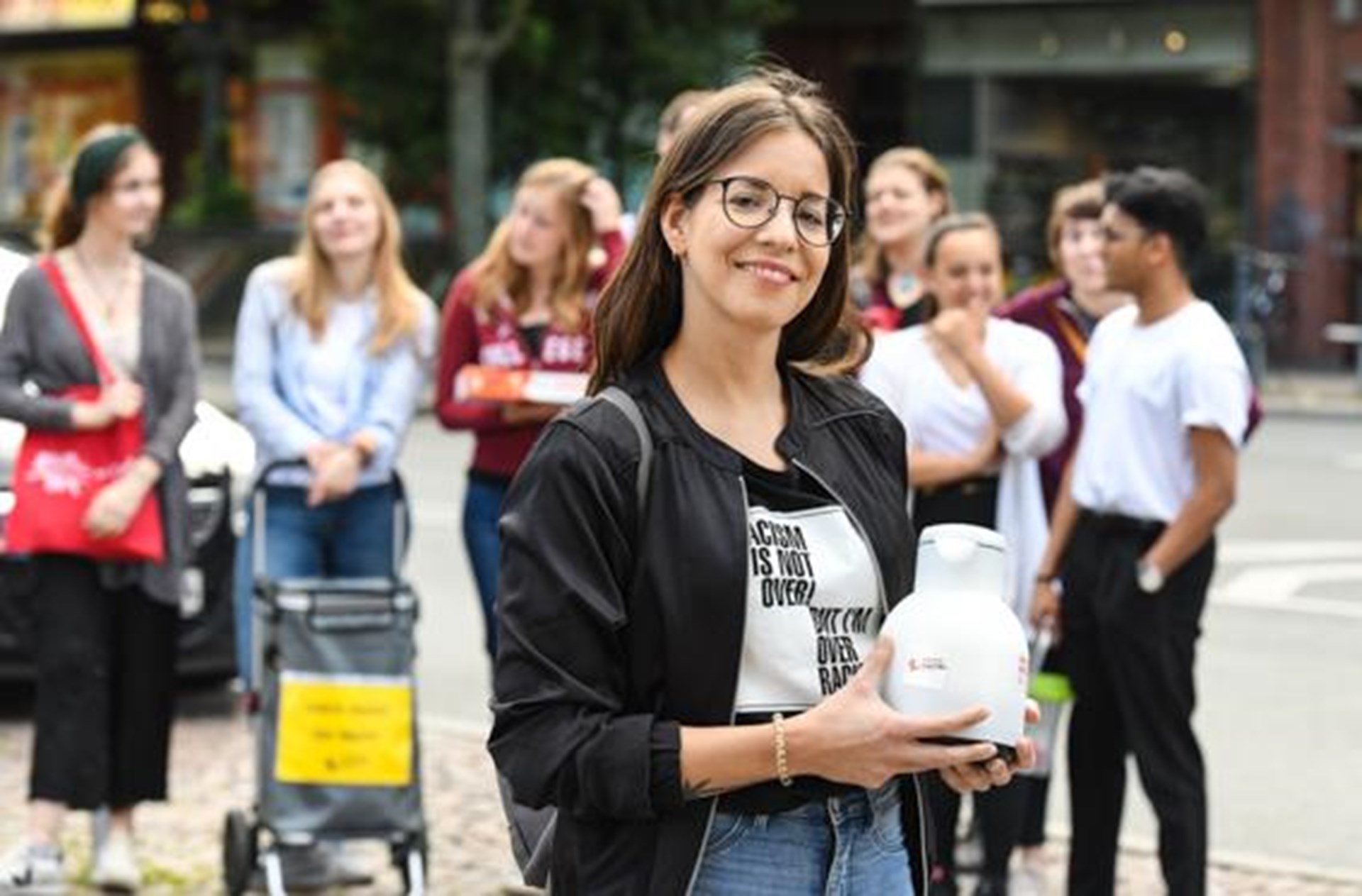 junge Frau mit schwarzen Haaren und Brille mit Thermoskanne im Arm