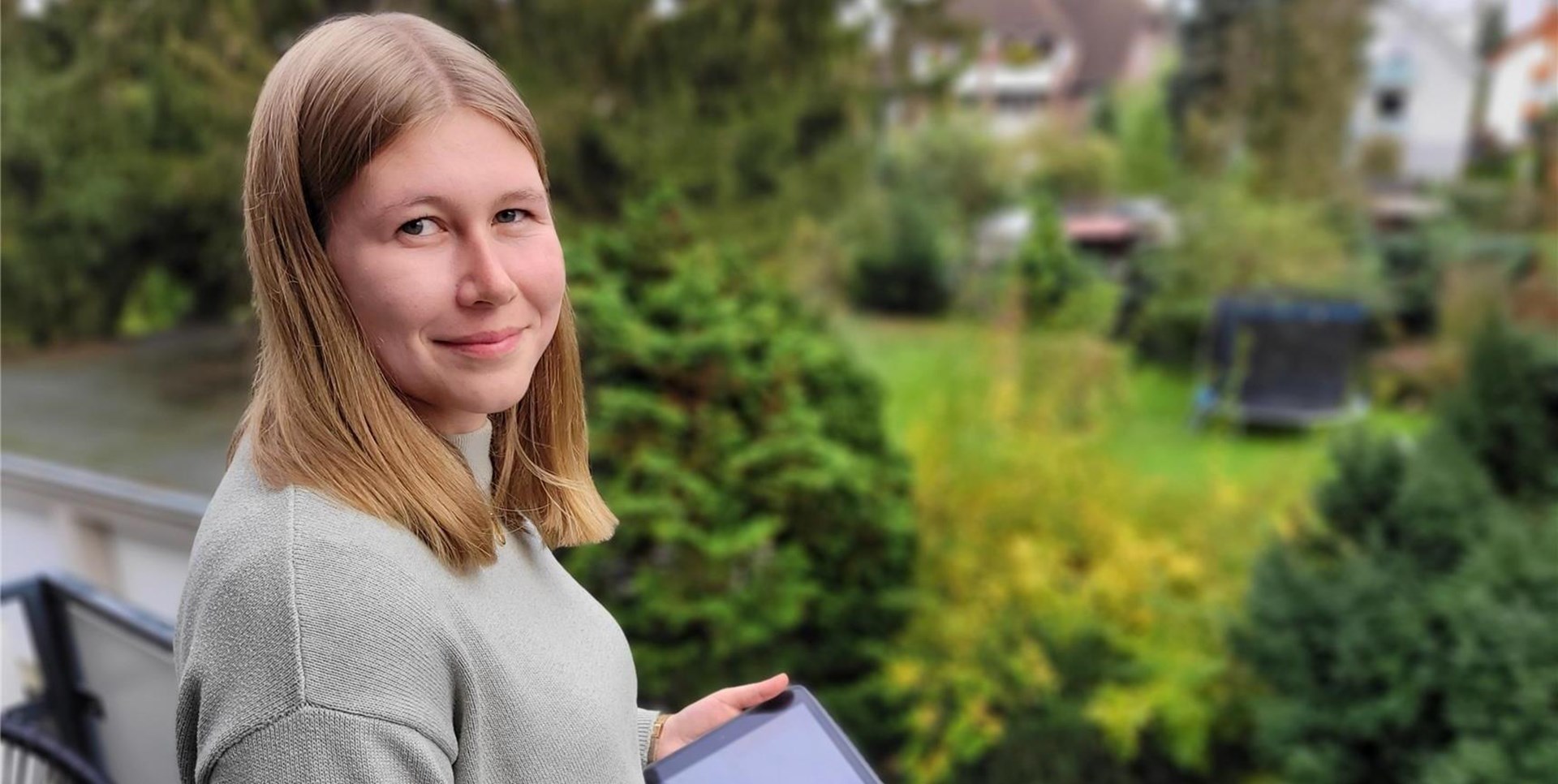 Junge Frau steht im Freien und hält ein Tablet in den Händen
