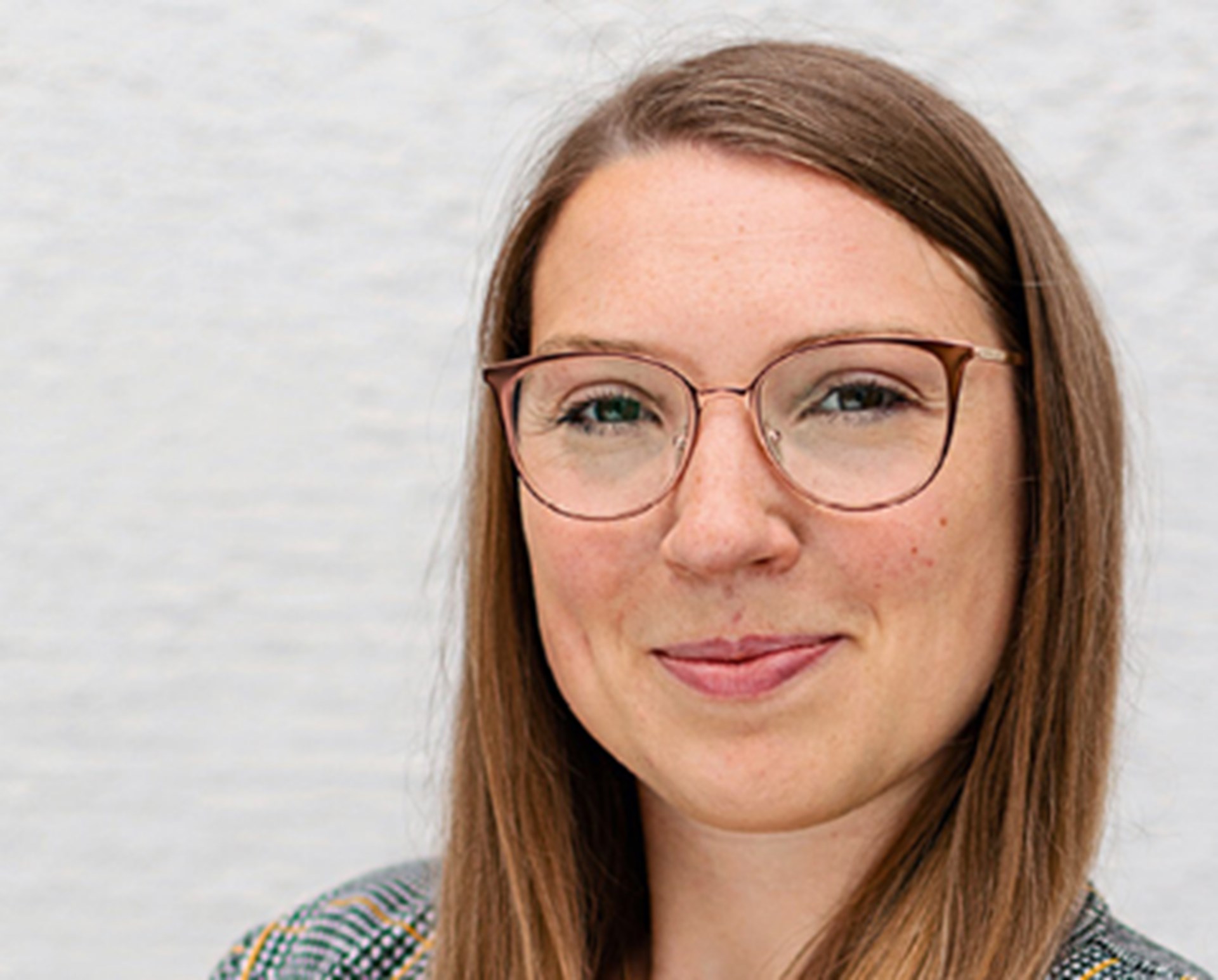 Sanft lächelnde Frau mit Brille, die eine grau-karierte Anzugjacke trägt