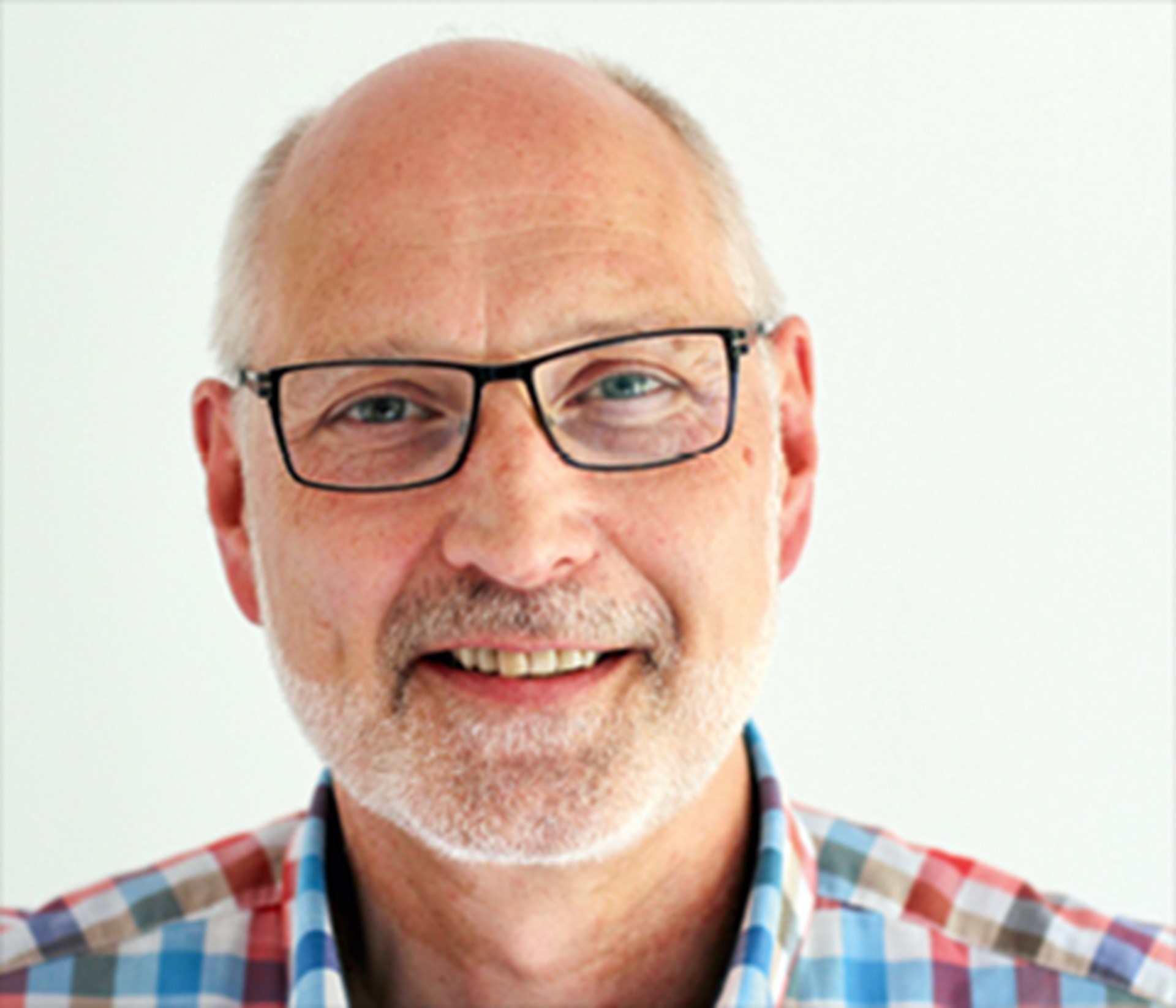 Lächelnder Mann mit grauen Haaren, Halbglatze, Vollbart und Brille, der ein kariertes Hemd trägt