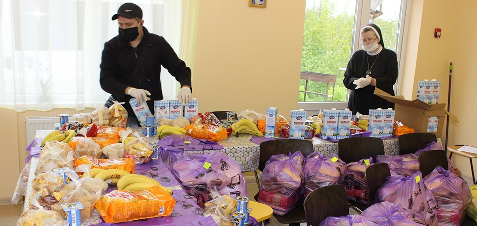 Eine Nonne und ein Mitarbeiter des Caritas-Sozialzentrums in Mamonowo packen in einem Raum Lebensmitteltaschen. Die dafür bereitgestellten Lebensmittel stehen auf langen Tischen.