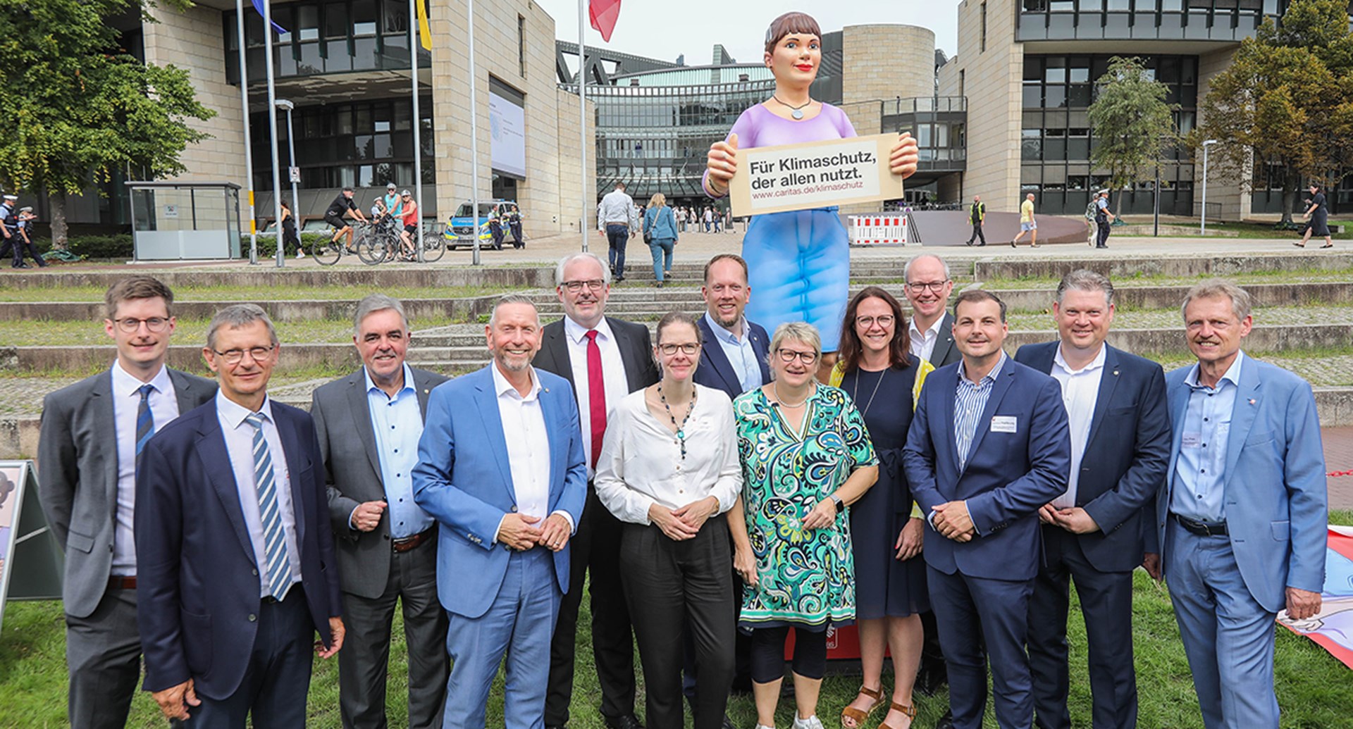 Ein Gruppenfoto mit Teilnehmenden einer Kundgebung vor dem Düsseldorfer Landtag und der Figur 'Jenny'