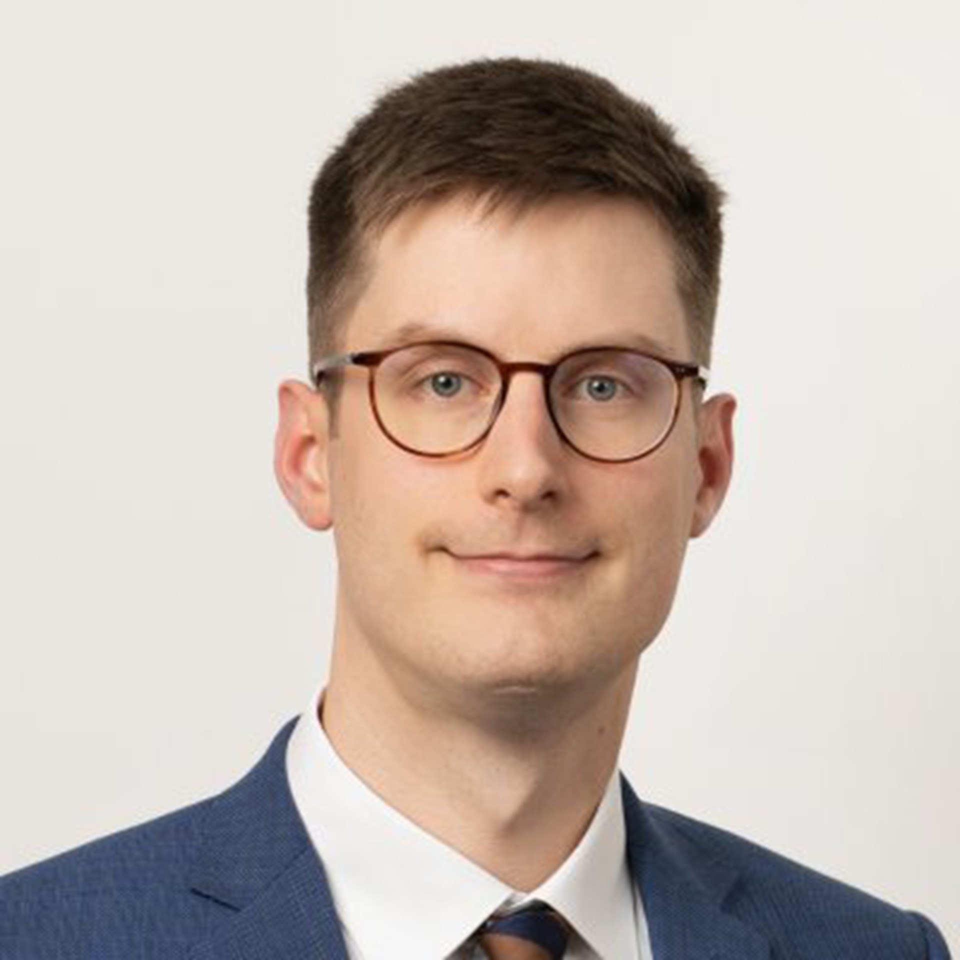 Lächelnder Mann mit blonden Haaren und Brille, der ein weißes Hemd mit einer blauen Anzugjacke und eine gestreifte Krawatte trägt