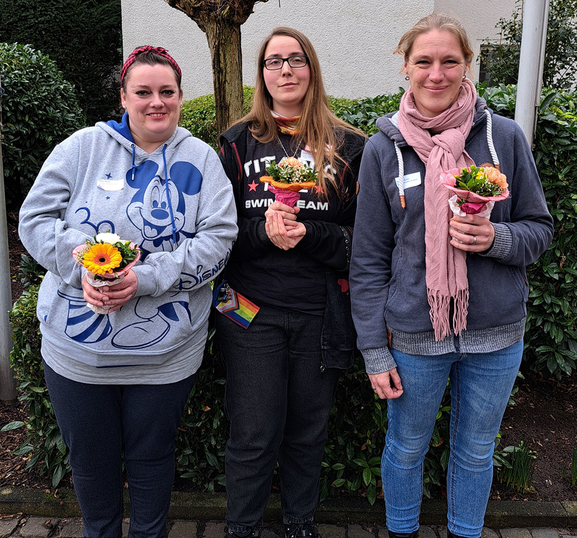 Die drei Delegierten der Frauenbeauftragten der Caritas in NRW nach ihrer Wahl in 2026, die mit Blumensträußen vor einer Hecke stehen.