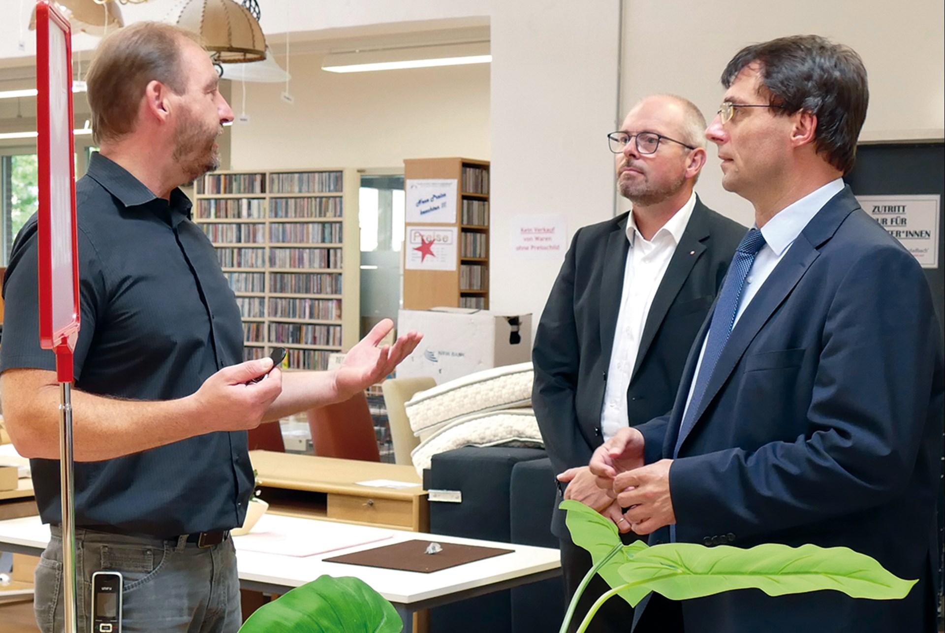 Der NRW-Finanzminister und ein Diözesan-Caritasdirektor stehen mit dem Vertriebsleiter in den Räumlichkeiten des Volksvereins Mönchengladbach und reden miteinander
