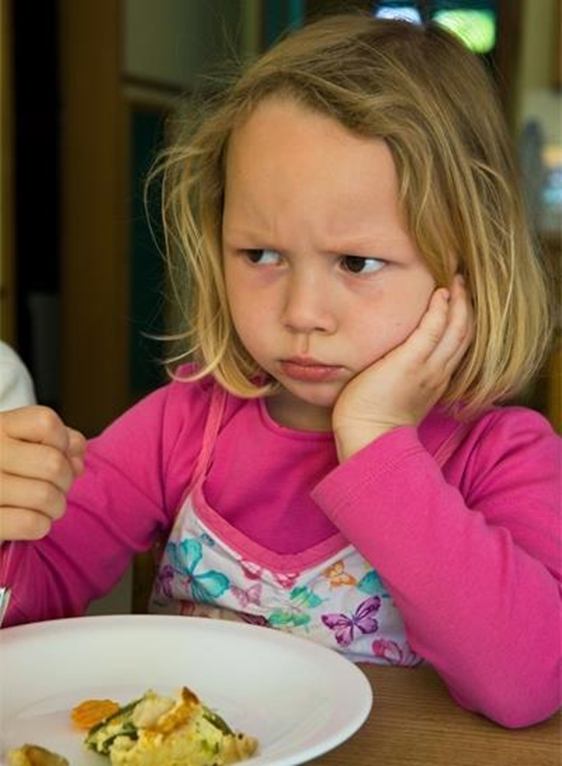 Ein Mädchen sitzt beim Mittagessen in einer trotzigen Pose vor ihrem halb gefüllten Teller