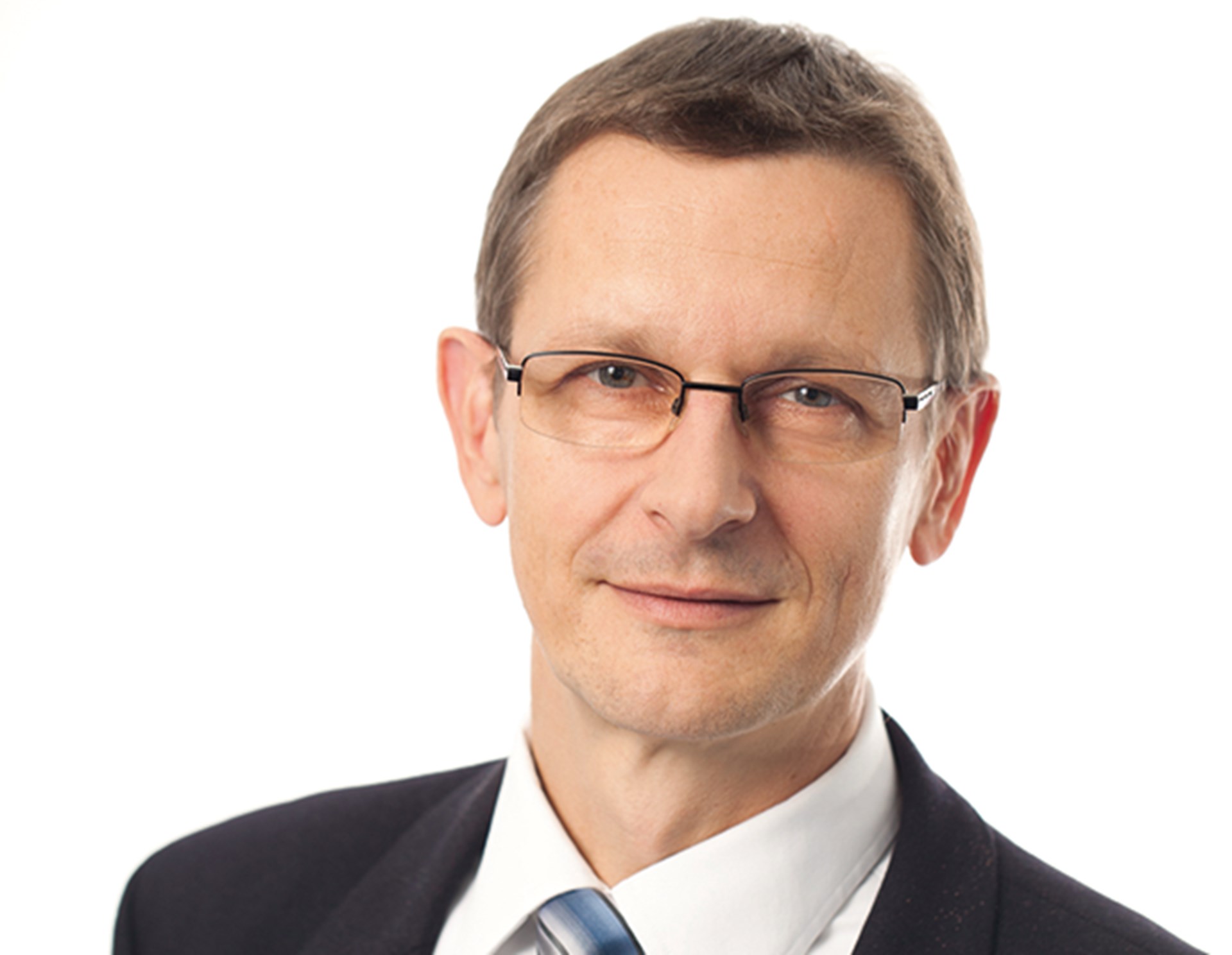 Lächelnder Mann mit braunen Haaren und Brille, der ein weißes Hemd, eine gestreifte Krawatte und eine schwarze Anzugjacke trägt