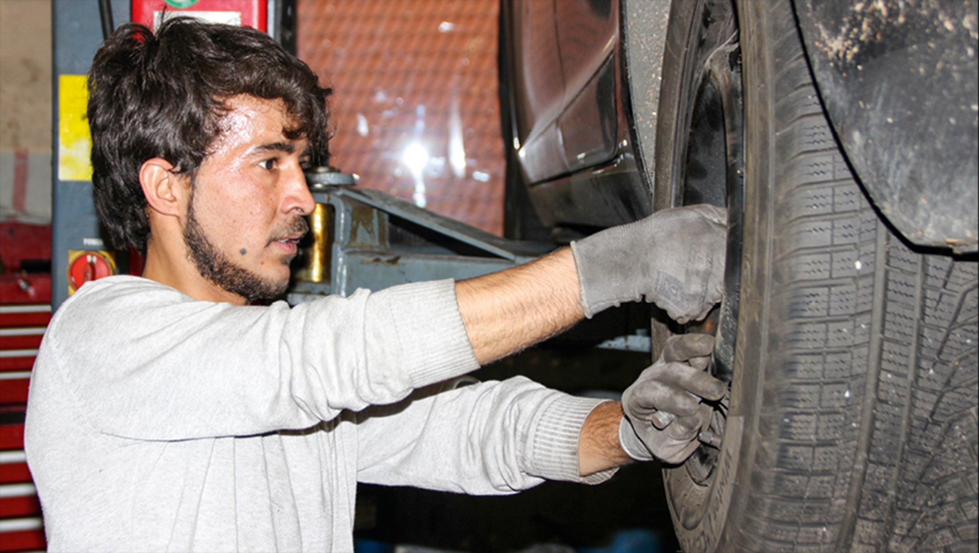 Ein Auszubildener mit Fluchthintergrund hantiert in einer Autowerkstatt an einem Rad herum