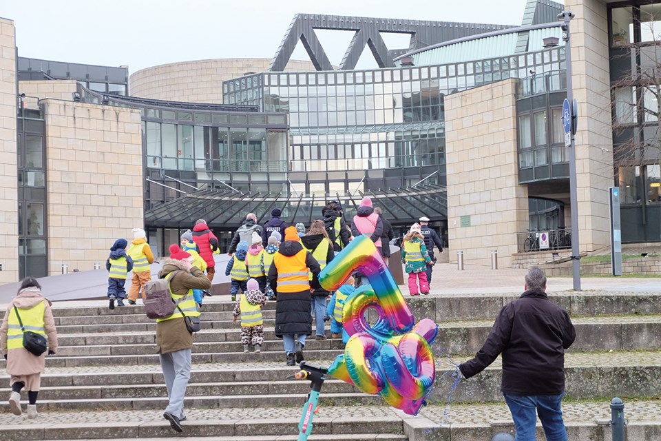 Eine Gruppe von Erwachsenen und Kindern laufen die Treppen zum Eingang des Düsseldorfer Landtags nach oben und stehen damit mit dem Rücken zur Kamera. Ein Mann hält dabei bunte Luftballons in der linken Hand.