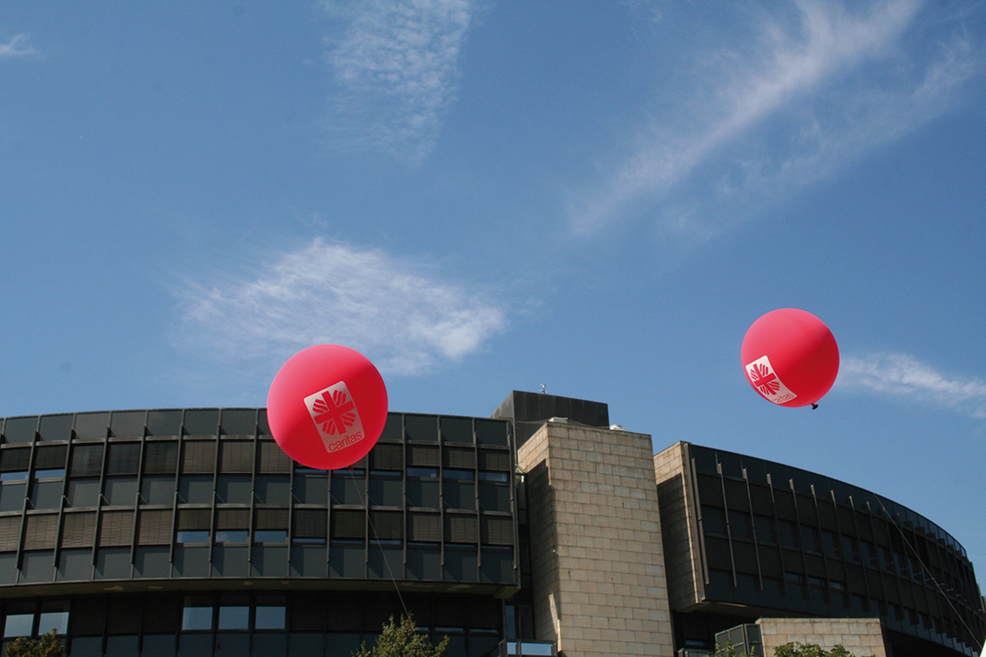 Zwei Caritas-Luftballons, die am wolkenlosen Himmel vor dem Landtagsgebäude in Düsseldorf schweben