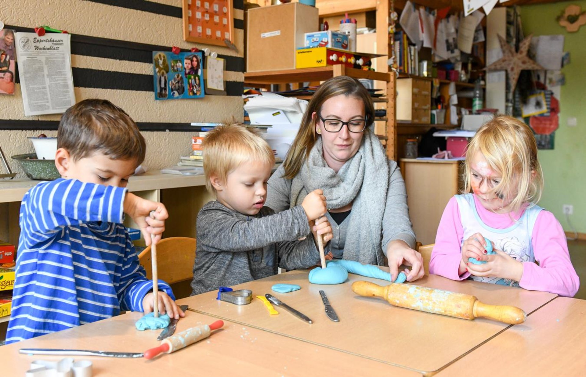 Drei Kinder und eine Frau sitzen am Tisch und kneten.