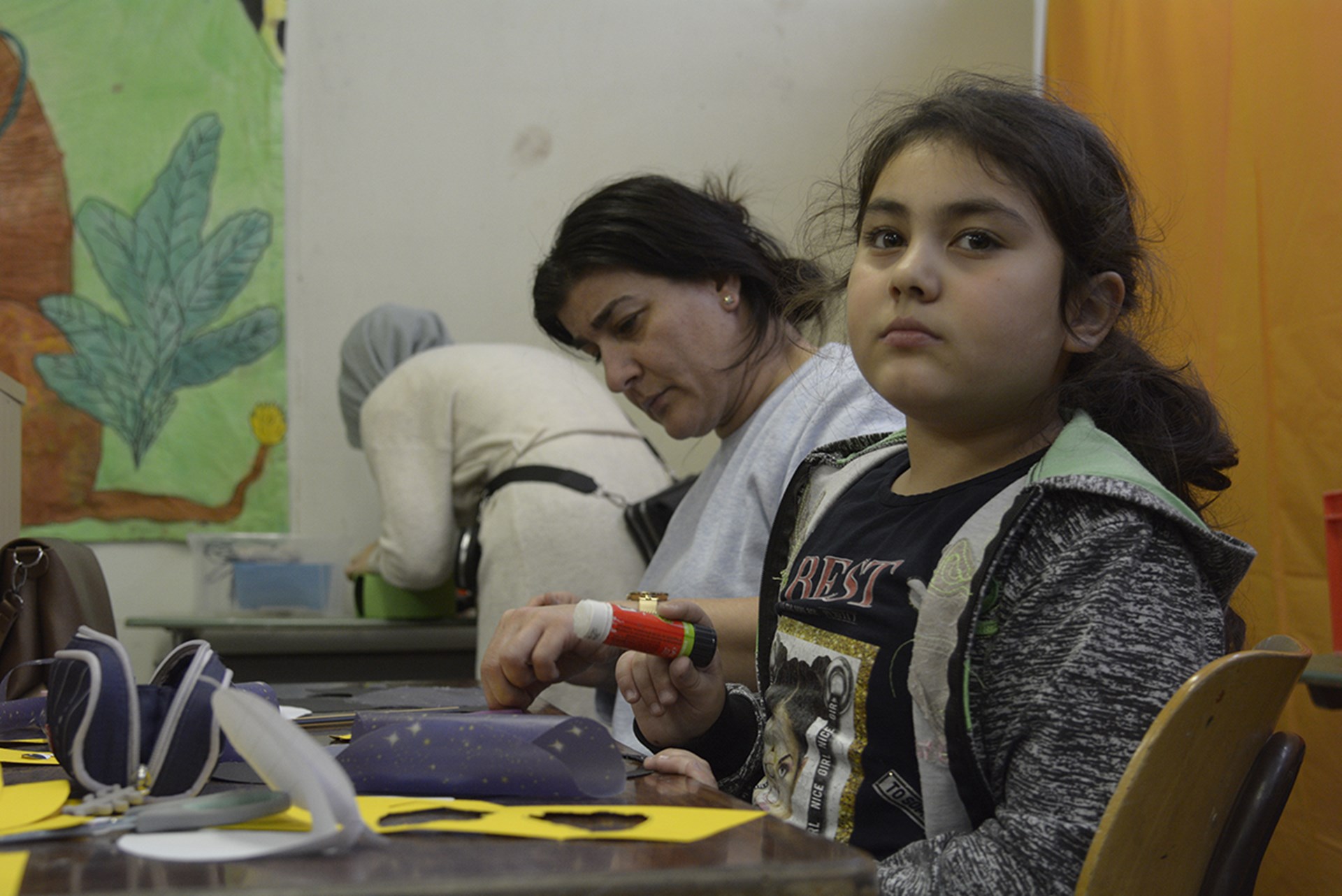 Ein Mädchen sitzt in der Brüder-Grimm-Schule in Mülheim an der Ruhr bei einem Bastelnachmittag zusammen an einem Tisch und bastelt. Im Hintergrund steht eine weitere Frau.