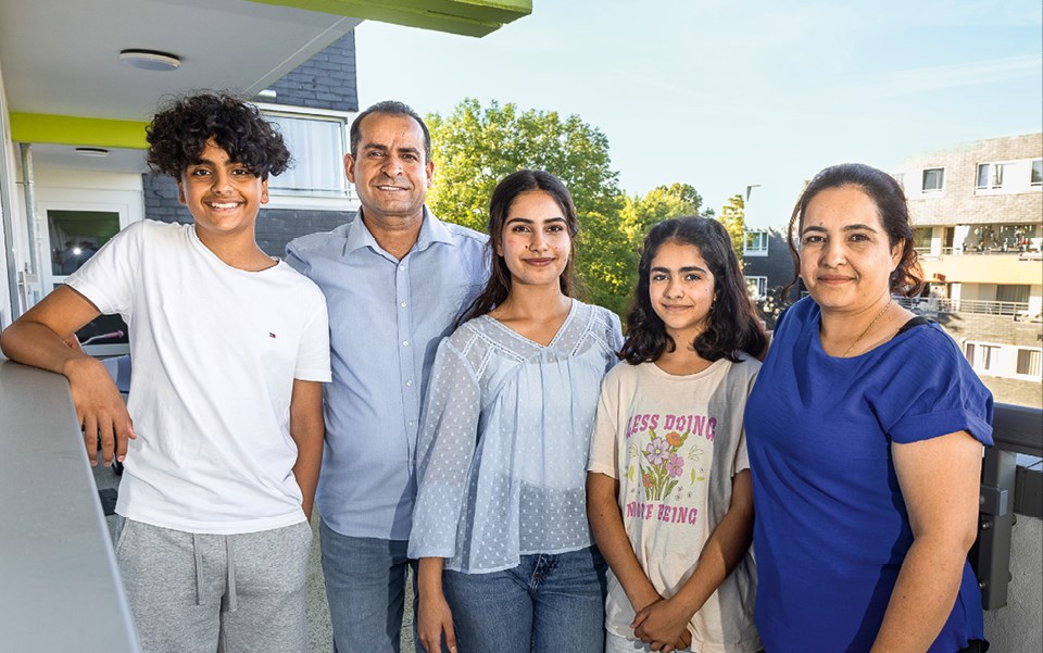 Eine fünfköpfige Familie steht zusammen in einem Laubengang des Wohnhauses, in dem sie leben