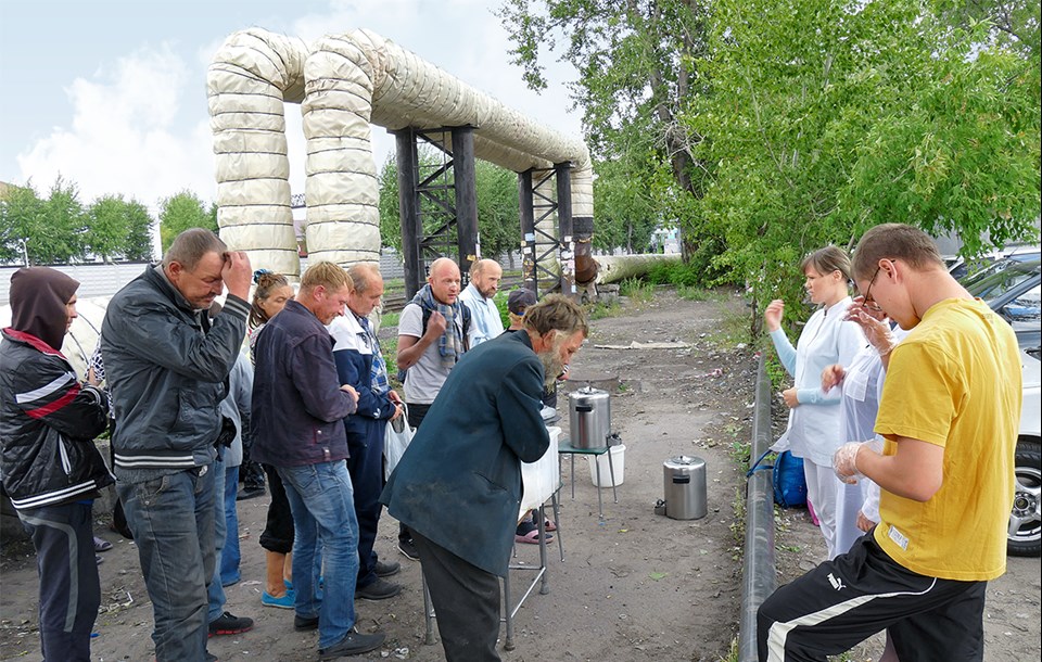 Russische Obdachlose stehen mit Mitarbeiterinnen der Caritas vor einer provisorischen Essenausgabe hinter einem Bahnhofsgelände und beten