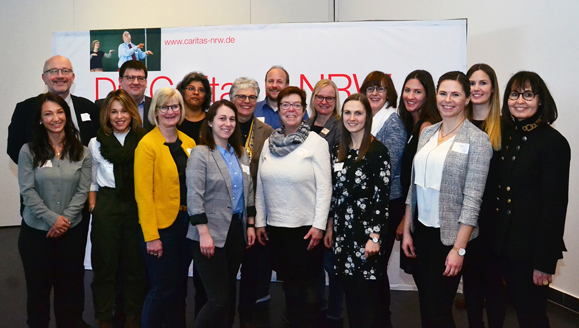 Ein Gruppenbild mit den Vertretenden des Projekts 'Phase L' bei der Abschlussveranstaltung am 13. Februar 2020 in Bochum vor einem Faltdisplay der Caritas in NRW