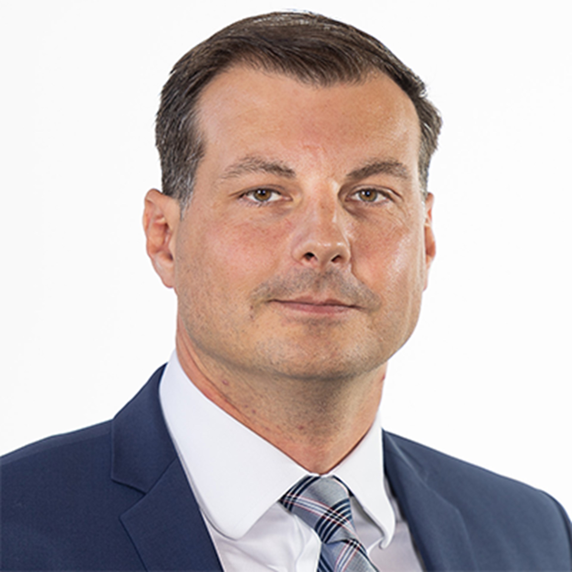 Sanft lächelnder Mann mit braunen Haaren, der ein weißes Hemd, eine karierte Krawatte und eine blaue Anzugjacke trägt