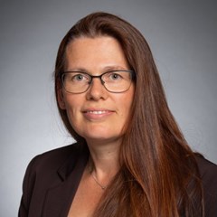 Lächelnde Frau mit langen, braunen Haaren, die eine schwarze Anzugjacke trägt