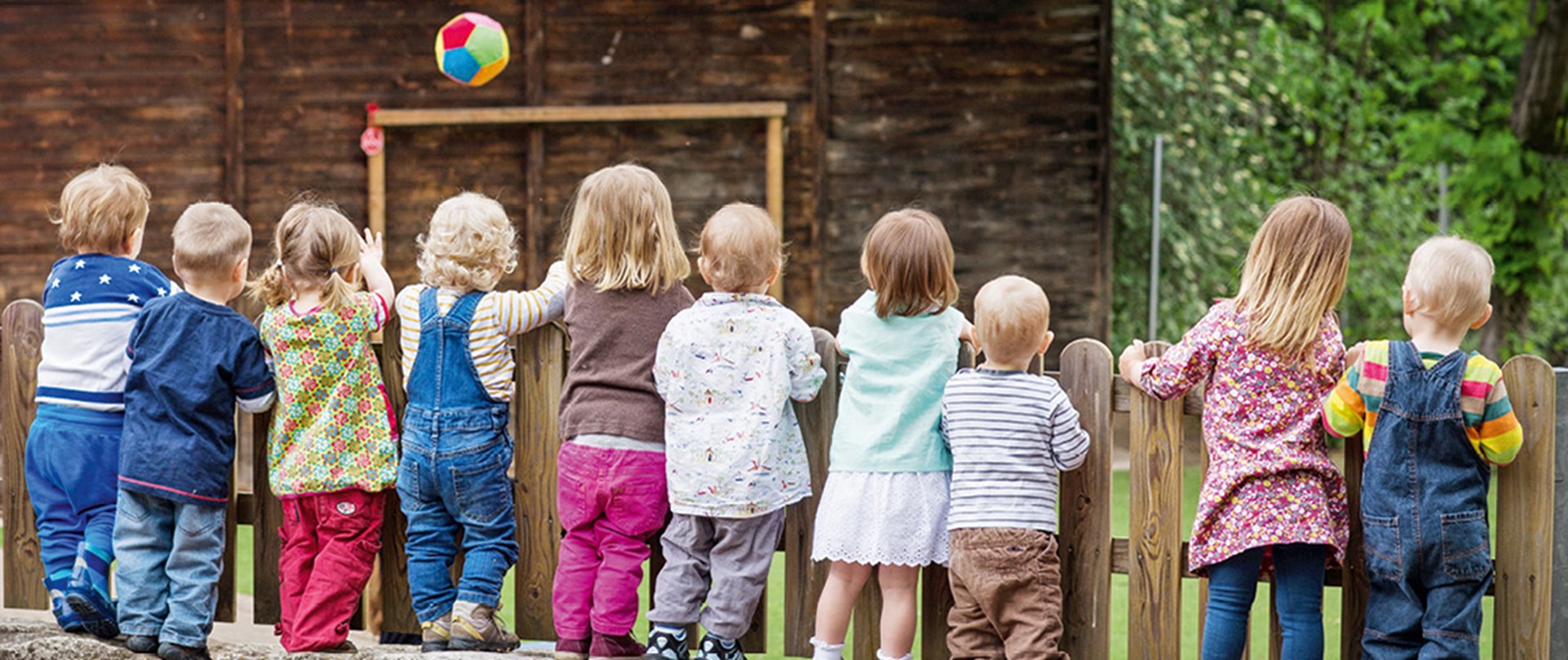 Eine Gruppe von Kindern steht an einem Zaun und beobachtet ein Fußballspiel