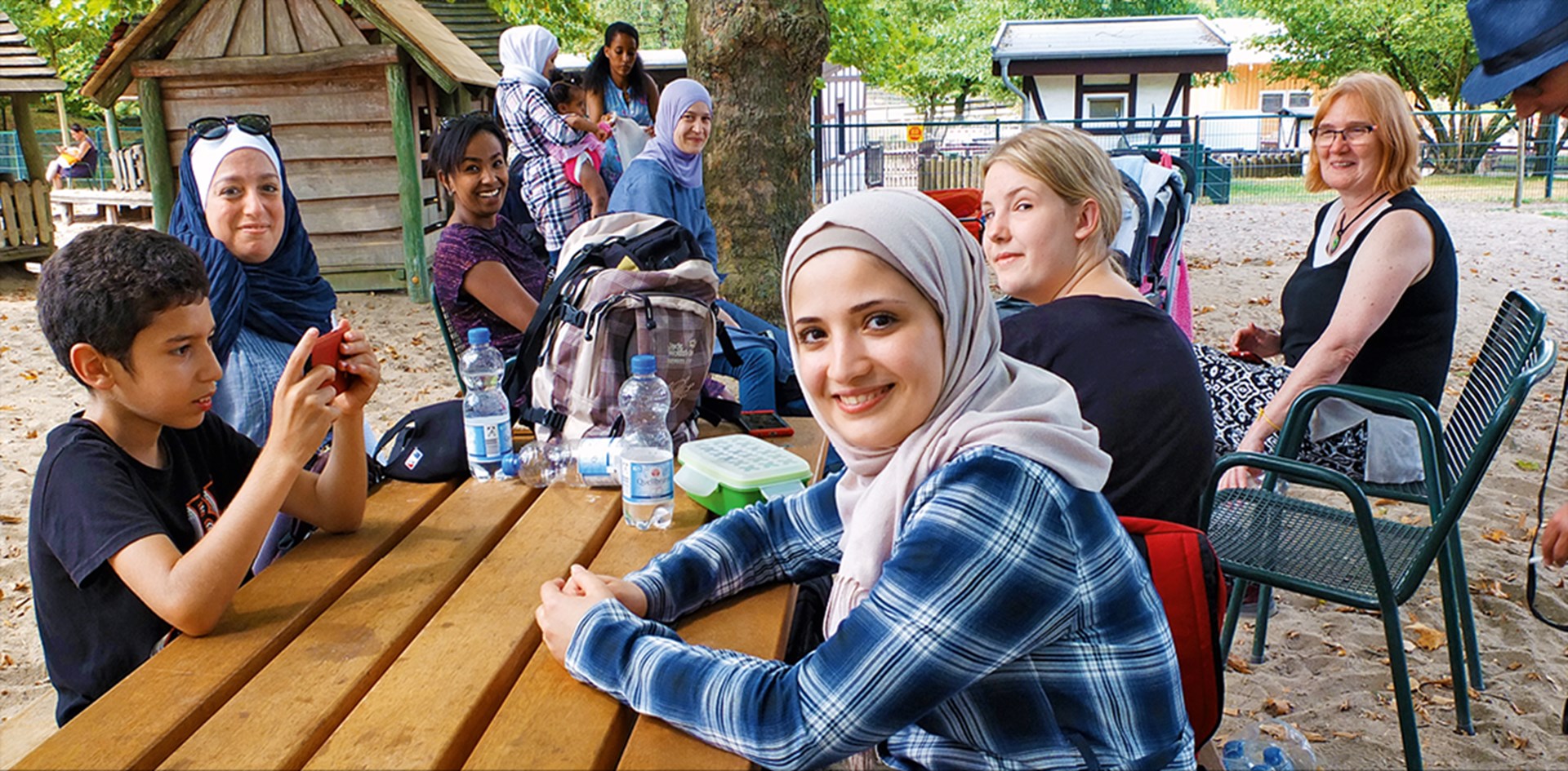 Eine Gruppe von acht Frauen sitzt mit zwei Kindern auf einem Spielplatz in der Essener Gruga zusammen