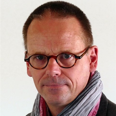 Mann mit braunen Haaren und Brille, der einen grau-pinken Schal trägt