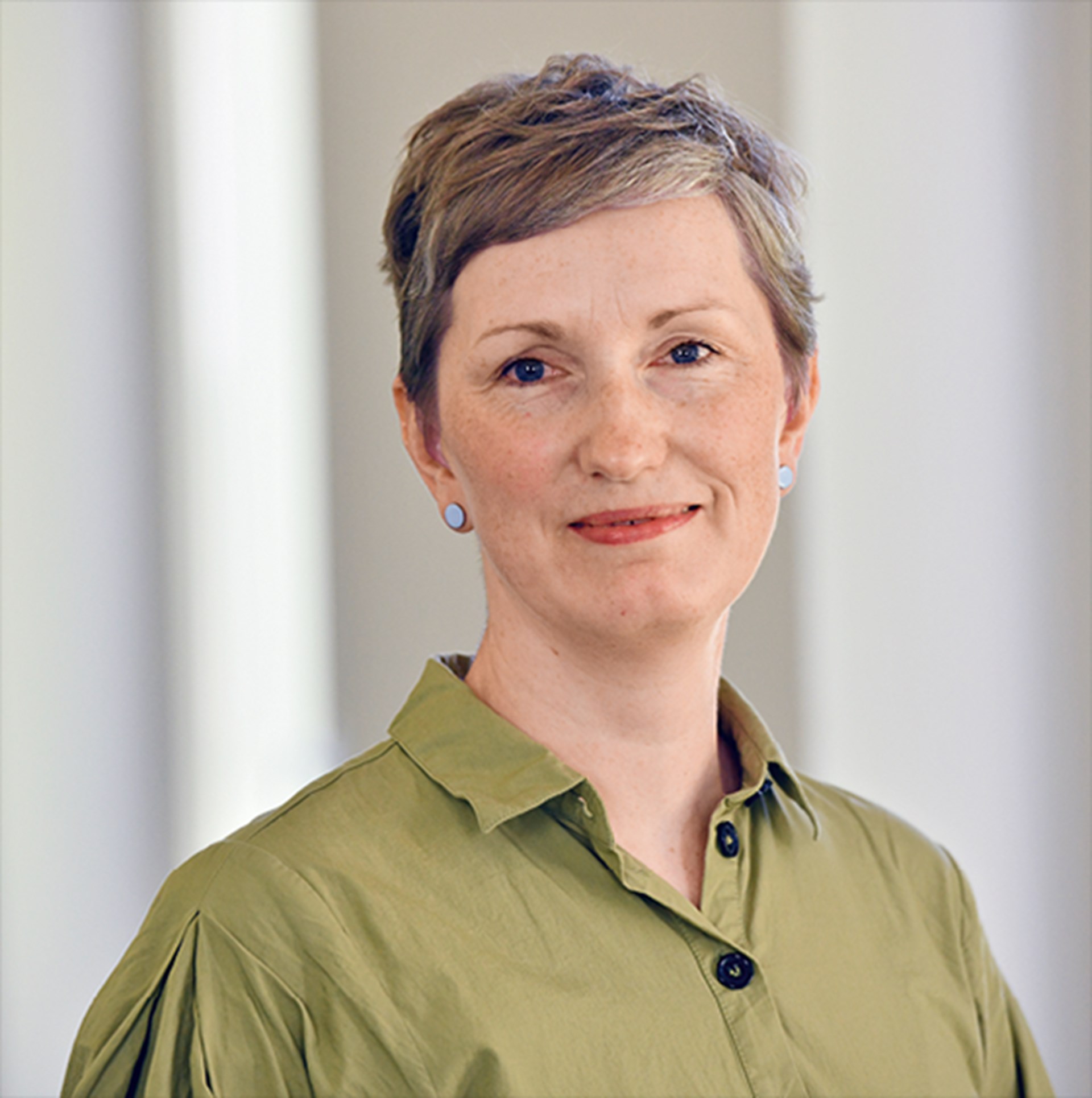 Sanft lächelnde Frau mit braun-grauen Haaren, die ein grünes Hemd trägt