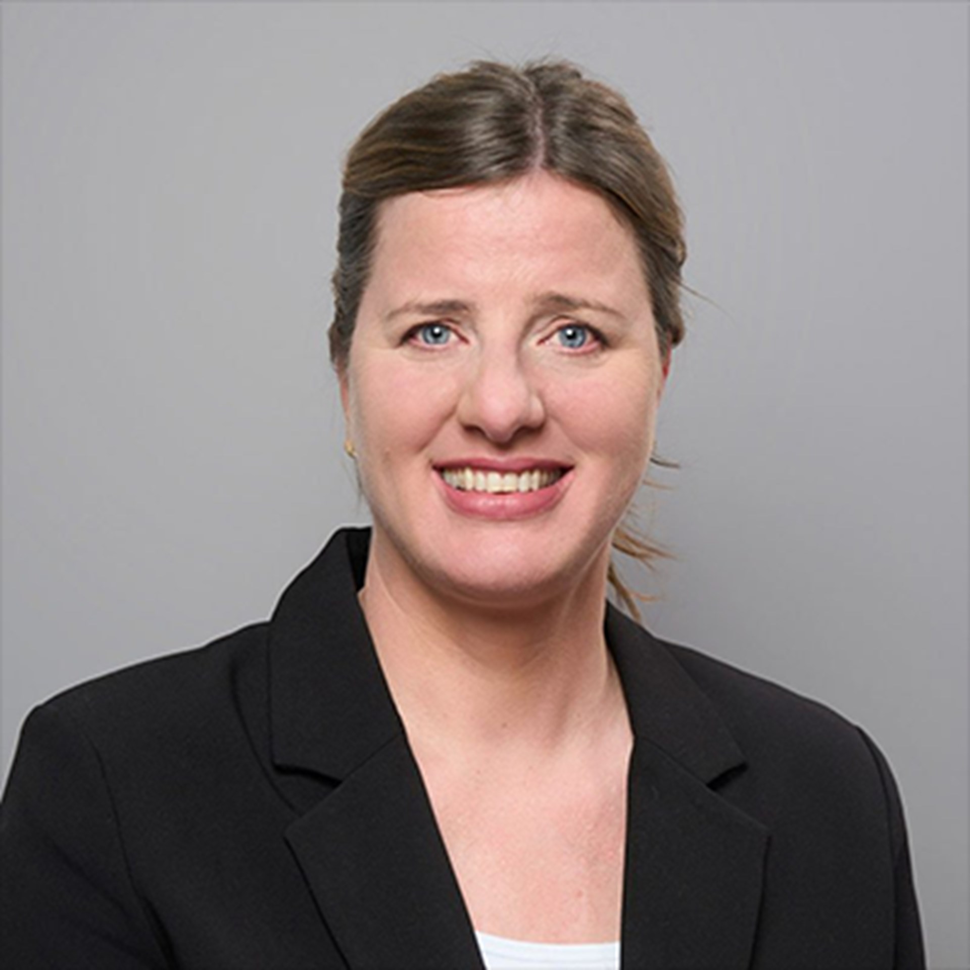 Lächelnde Frau mit blonden Haaren, die ein weißes Shirt und eine schwarze Anzugjacke trägt.