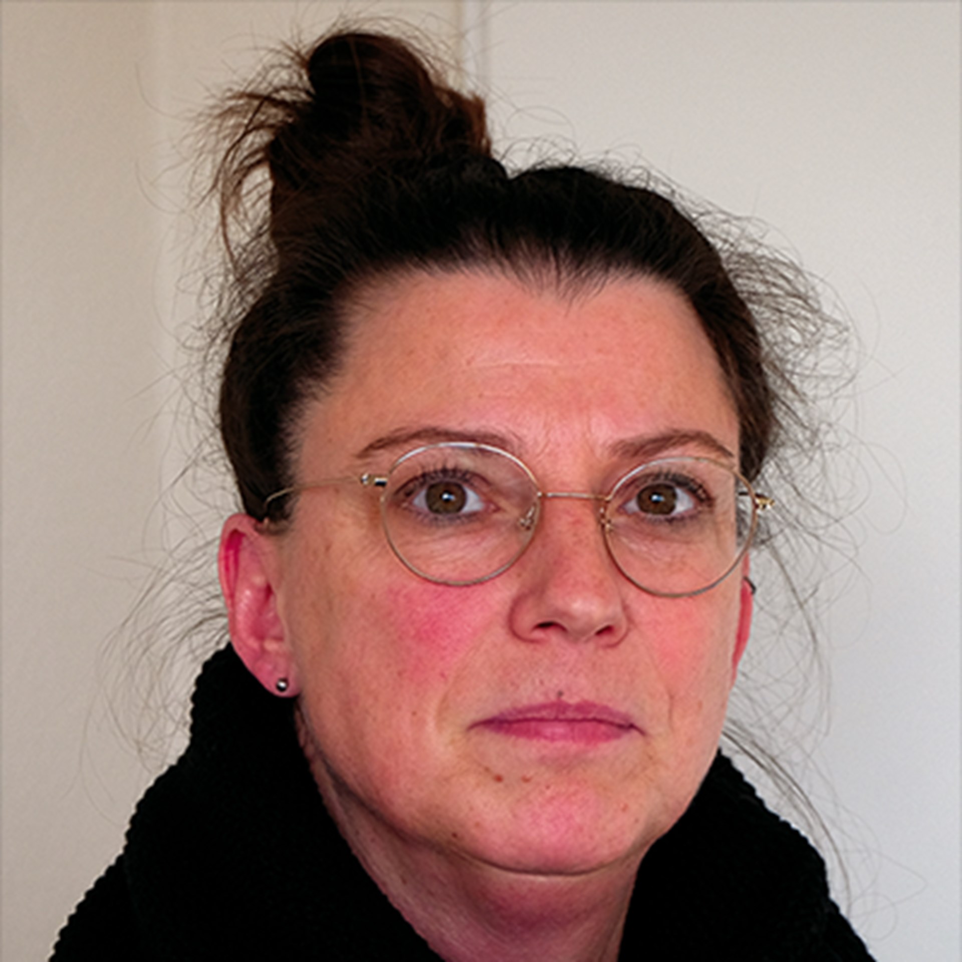 Frau mit dunkel-braunen, zu einem Dutt zusammengebundenen Haaren und einer Brille, die ein schwarzes Oberteil trägt