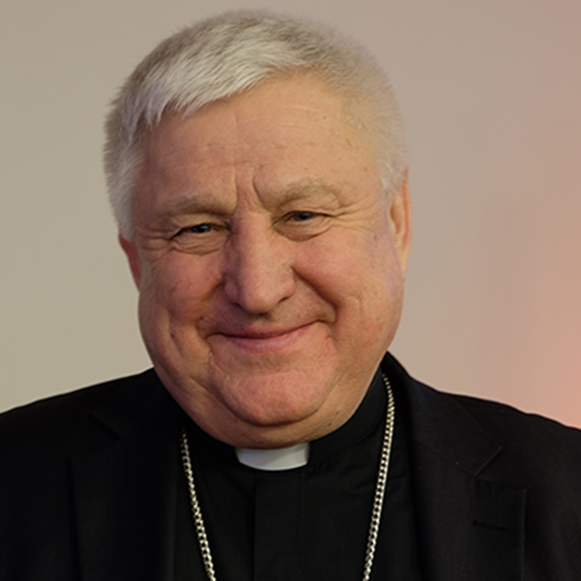Lächelnder, älterer Mann mit grauen Haaren, der eine schwarze Priesterkleidung (Soutane) trägt