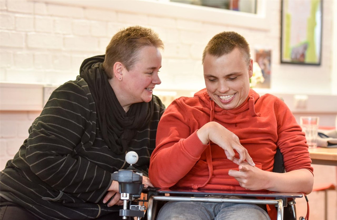 Eine Frau sitzt neben einem jungen Mann im Rollstuhl. 
