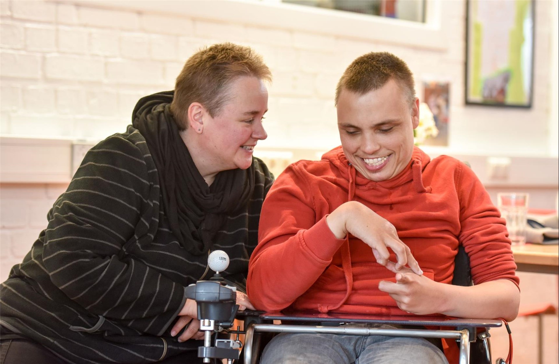 Eine Frau sitzt neben einem jungen Mann im Rollstuhl. 