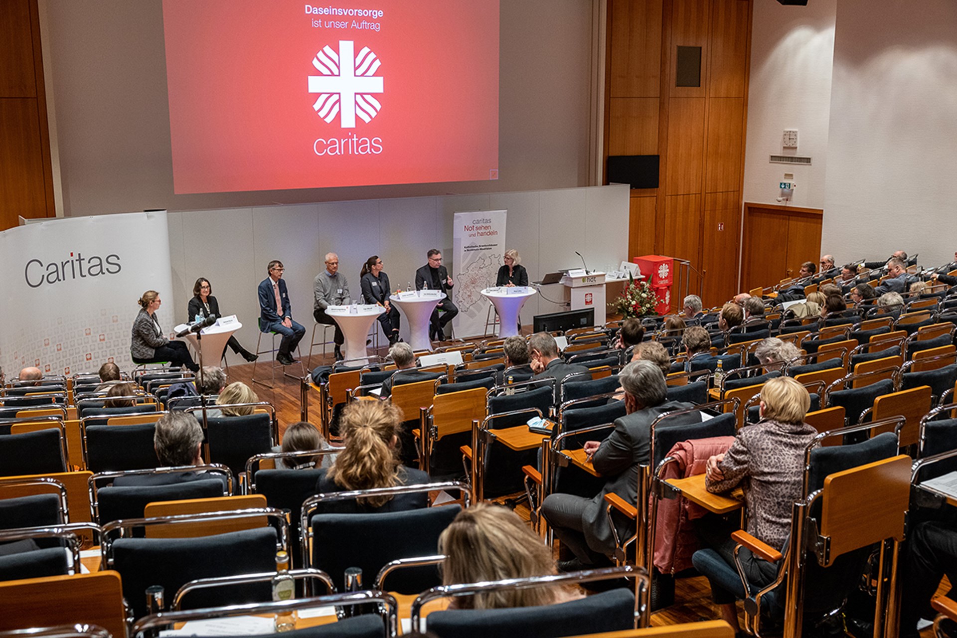 Podiumsdiskussion beim 1. Kath. Krankenhaustag NRW in Essen, bei der im Vordergrund das Publikum zu sehen ist. Im Hintergrund sieht man eine Leinwand.