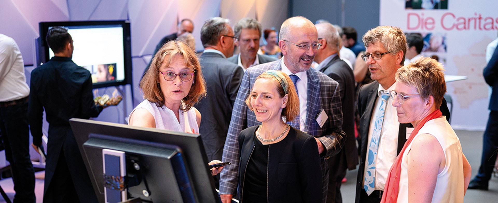 Teilnehmenden des Parlamentarischen Abends der Caritas in NRW in Berlin, die sich beim Gallery Walk digitale Projekte und Errungenschaften der Caritas ansehen