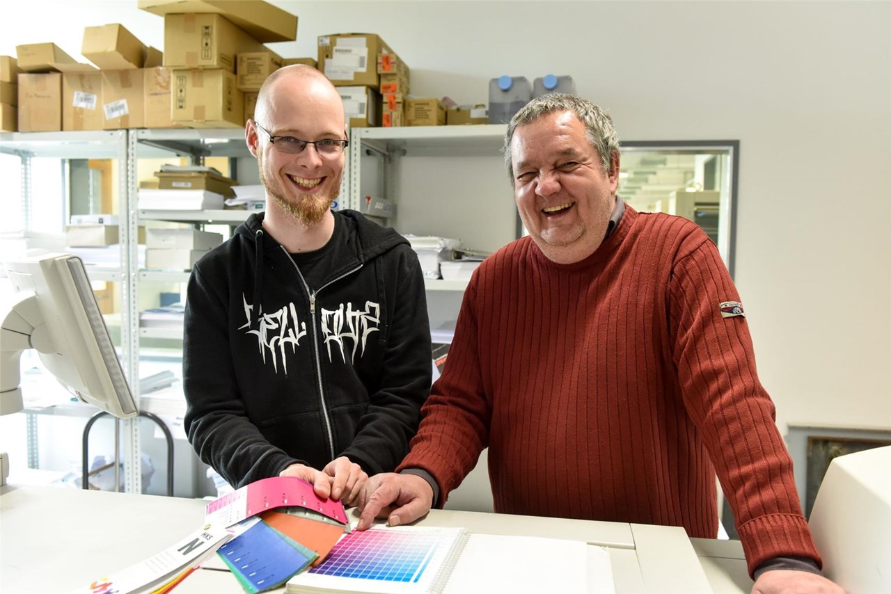 Betreuer und Mann mit Behinderung lachen stehend in die Kamera