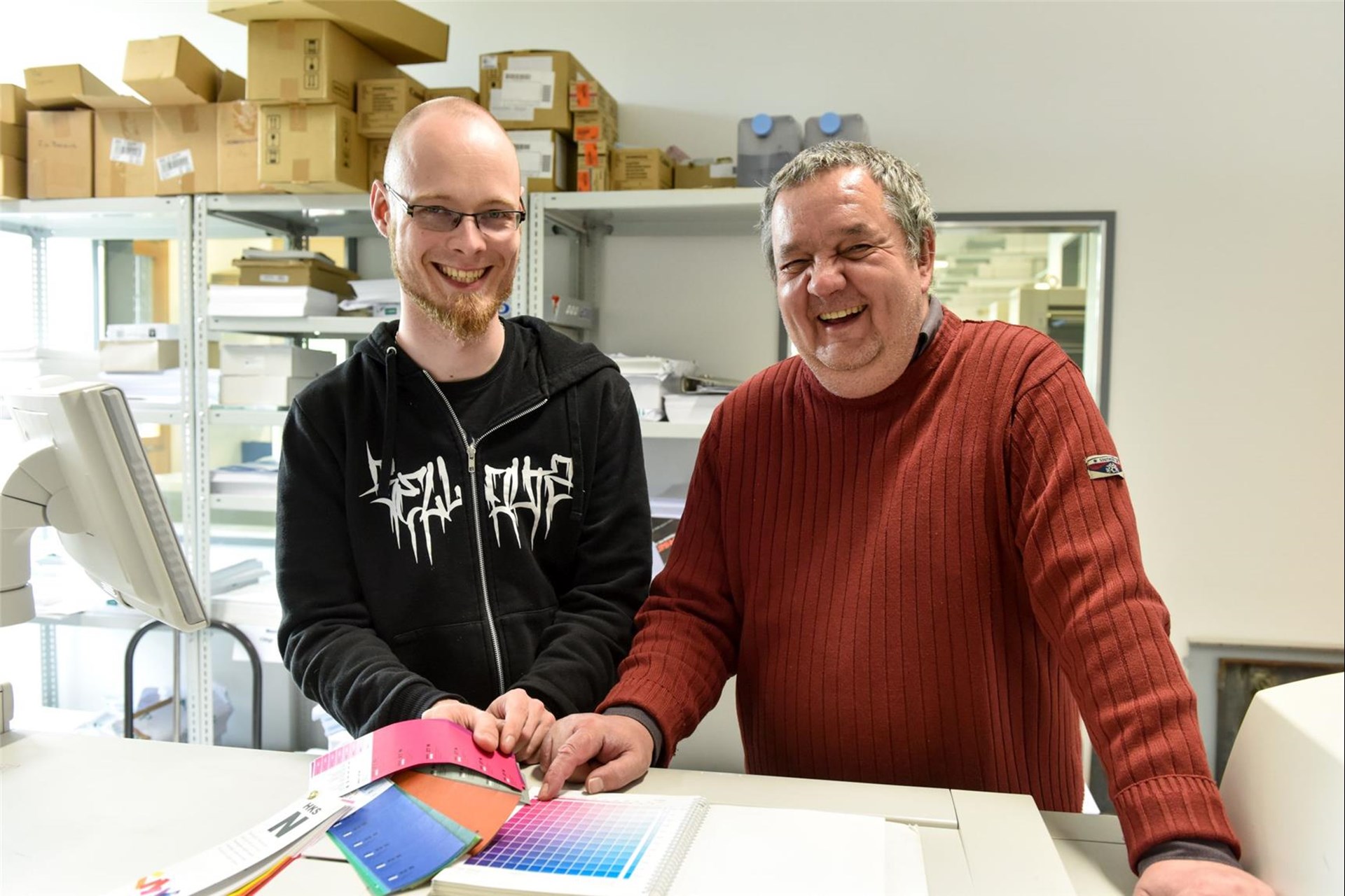 Betreuer und Mann mit Behinderung lachen stehend in die Kamera