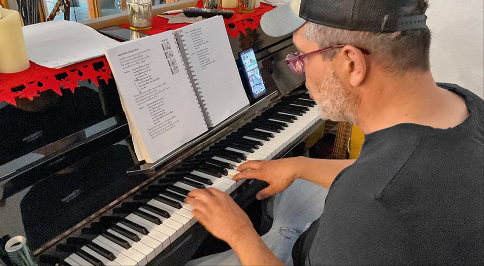 Ein Mann sitzt an einem schwarzen Keyboard vor einem Notenbuch und spielt. Die Oberseite des Klaviers ist weihnachtlich dekoriert.