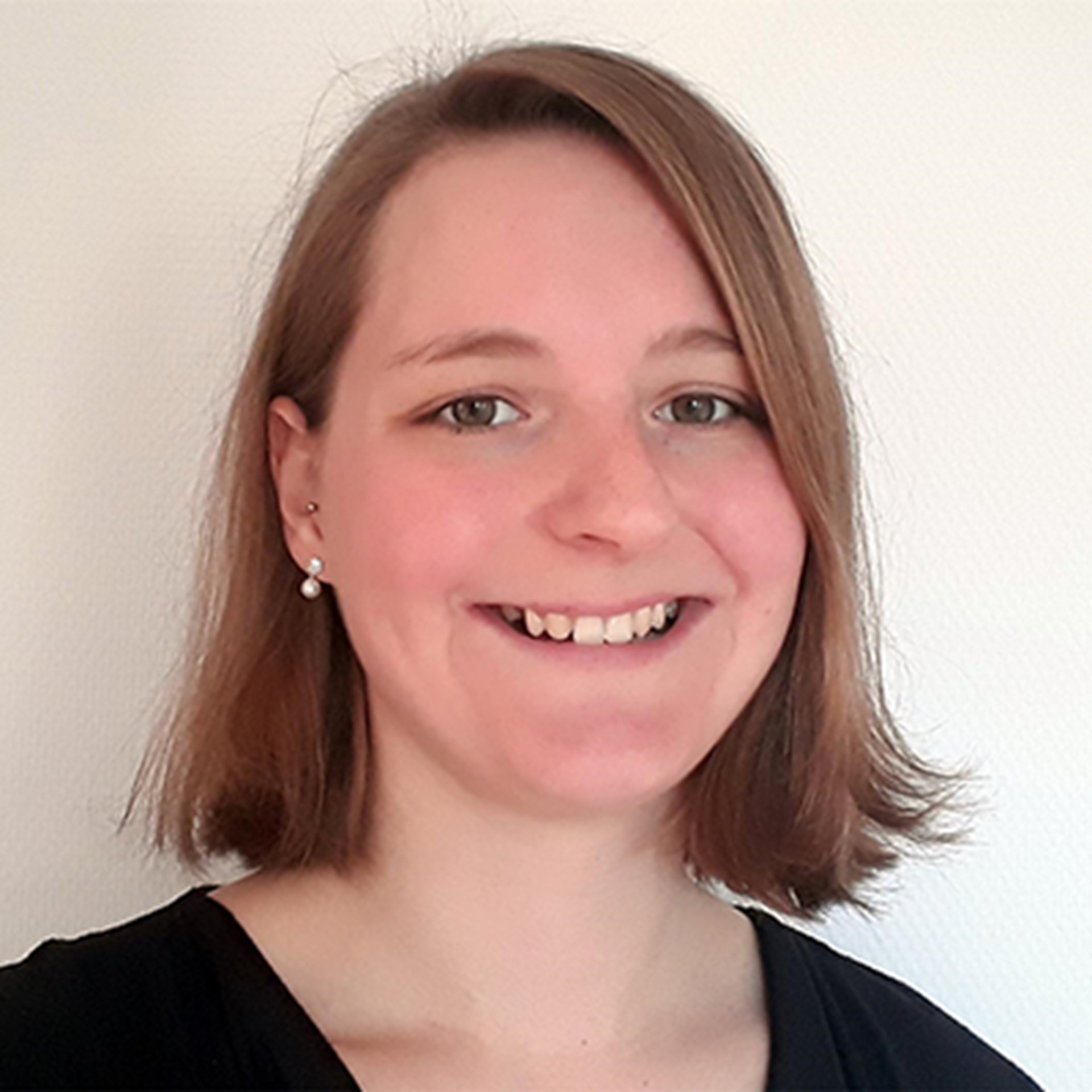 Lächelnde Frau mit schulterlangen, braunen Haaren, die ein schwarzes Shirt trägt.