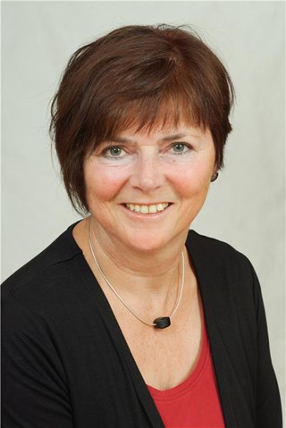 Lächelnde Frau mit braunen Haaren, die eine Kette mit einem schwarzen Stein, ein rotes T-Shirt und eine schwarze Jacke trägt